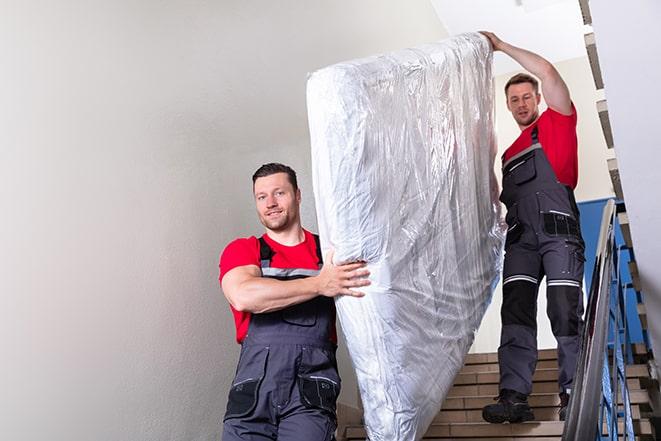 workers maneuvering a box spring through a narrow hallway in Weston